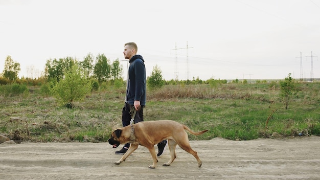 Junger sportlicher Mann, der nach dem Crossfit-Training mit seinem Bullmastiff-Hund im Freien in der Natur spazieren geht