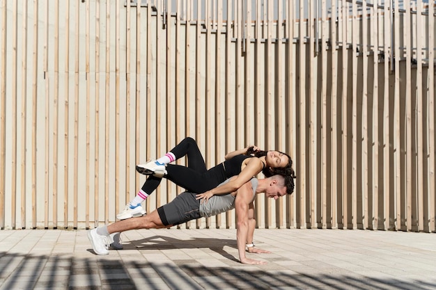 Junger sportlicher Mann in Plankenhaltung, der Frau auf dem Rücken trainiert und hält