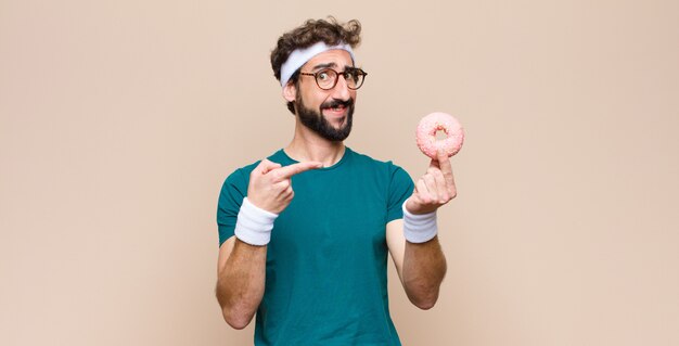 Junger Sportmann, der einen Snack hält, der einen rosa Zuckerkrapfen hält