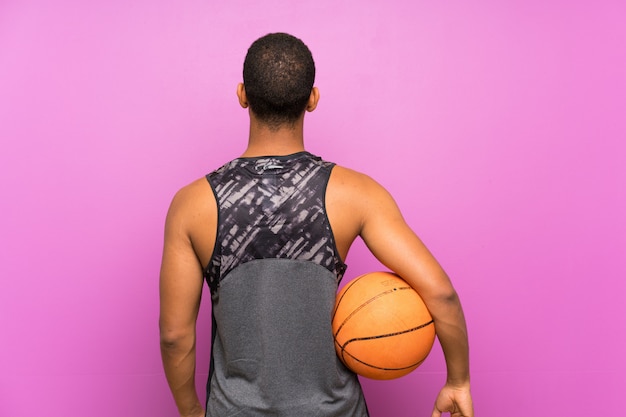 Junger Sportmann mit Ball des Basketballs über lokalisierter purpurroter Wand in hinterer Position