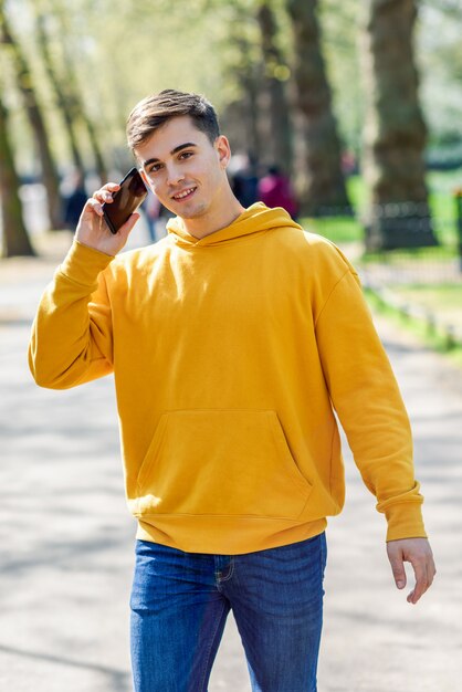 Junger städtischer Mann, der den Smartphone geht in Straße in einem städtischen Park in London verwendet.