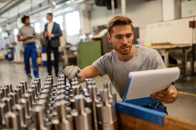 Foto junger stahlarbeiter, der die qualität der hergestellten stangenzylinder im industriegebäude überprüft