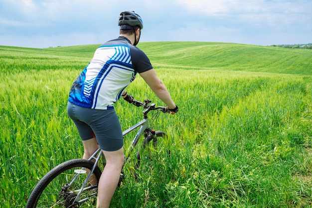 Junger starker Mann, der Fahrrad durch die grüne Wiese fährt