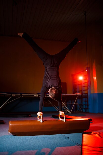 Junger starker Mann macht Handstandübungen. Männlicher Turner beim Sport in der Turnhalle