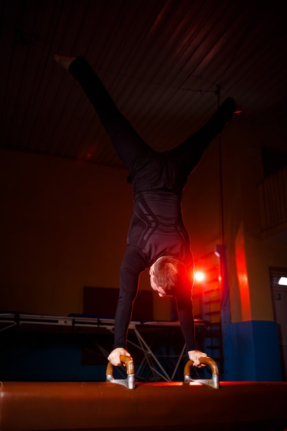 Junger starker Mann macht Handstandübungen. Männlicher Turner beim Sport in der Turnhalle