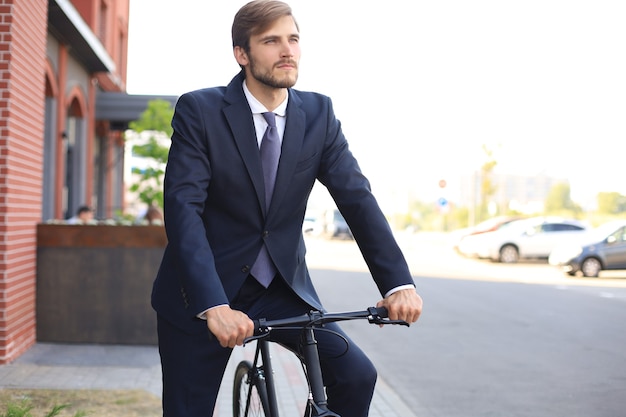 Junger, stilvoller Geschäftsmann im Anzug, der auf einem Fahrrad auf einer Stadtstraße fährt.