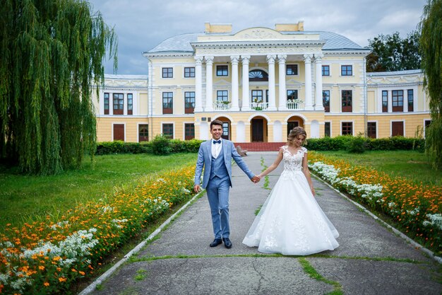 Junger stilvoller Kerl im Kostüm des Bräutigams und des schönen Mädchens der Braut in einem weißen Kleid mit einem Zugspaziergang im Park an ihrem Hochzeitstag wedding