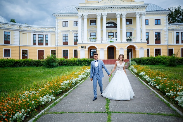 Junger stilvoller Kerl im Kostüm des Bräutigams und des schönen Mädchens der Braut in einem weißen Kleid mit einem Zugspaziergang im Park an ihrem Hochzeitstag