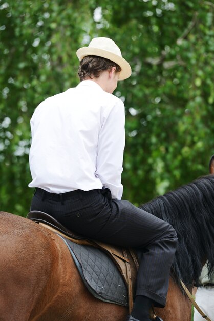 Foto junger stilvoller mann, der das reiten eines pferds auf landschaft nimmt