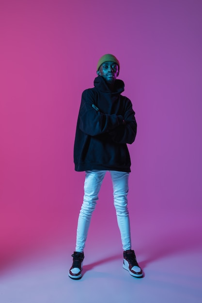 Junger stilvoller Mann im modernen Straßenstil-Outfit lokalisiert auf Steigungswand in Neonlicht-Afroamerikaner-Modemodell im Lookbook-Musiker, der durchführt