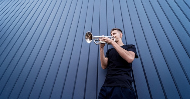 Junger Straßenmusiker, der die Trompete nahe der großen blauen Wand spielt