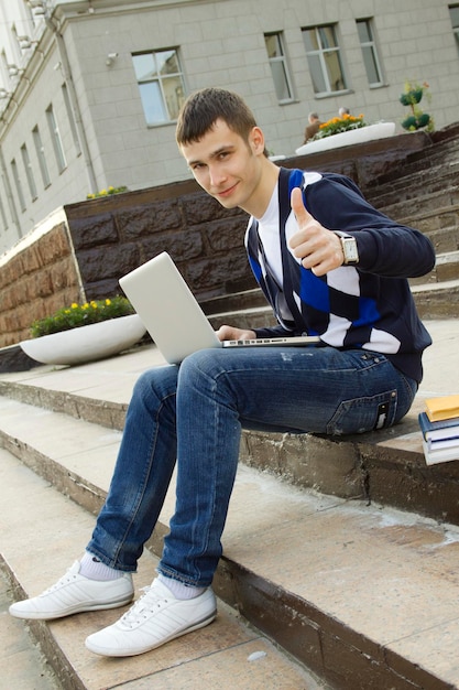 Junger Student, der an einem Laptop arbeitet Daumen hoch