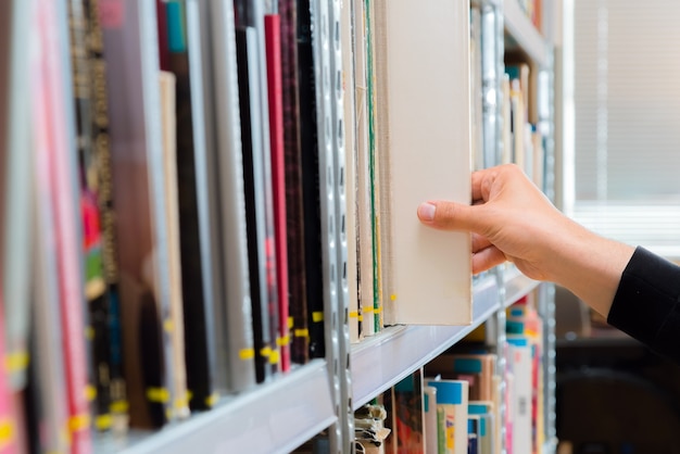 Junger Student, der ein Buch aus dem Regal in der Bibliothek auswählt.