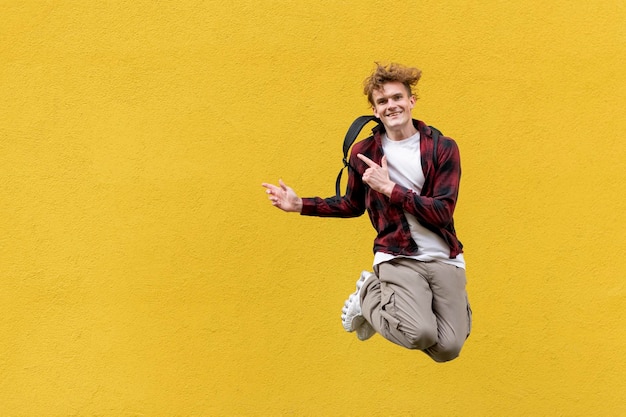 Junger Student mit Rucksack springt vor dem Hintergrund einer gelben, isolierten Wand