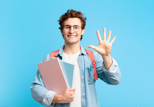 Junger Studentenjunge, der lächelt und freundlich aussieht, Nummer fünf oder fünf mit der Hand nach vorne zeigt, herunterzählt