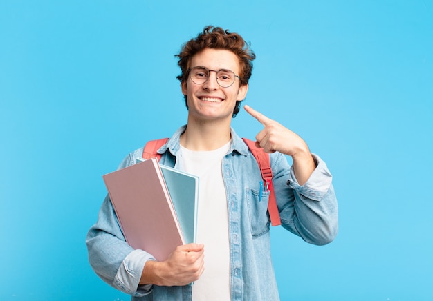 Junger Studentenjunge, der selbstbewusst auf sein eigenes breites Lächeln, positive, entspannte, zufriedene Haltung lächelt