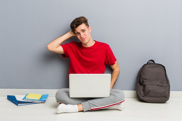 Junger Studentenmann, der auf seinem Hausboden hält einen Laptop sitzt