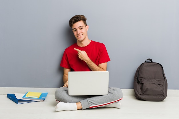 Junger Studentenmann, der auf seinem Hausboden hält einen Laptop sitzt