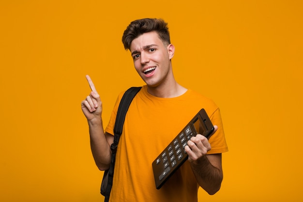 Junger Studentenmann, der einen Taschenrechner hält, der mit dem Finger auf Sie zeigt, als ob die Einladung näher kommt.