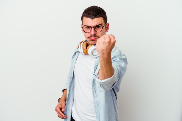 Junger Studentenmann, der Musik lokalisiert auf weißer Wand hört, die Faust nach vorne zeigt, aggressiver Gesichtsausdruck