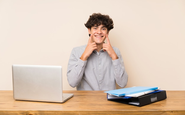 Junger Studentenmann mit einem Laptop lächelnd mit einem glücklichen und angenehmen Ausdruck