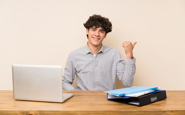 Junger Studentenmann mit einem Laptop zeigend auf die Seite, um ein Produkt darzustellen