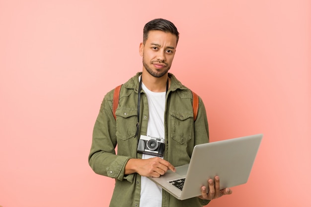 Junger südasiatischer Mann, der einen Laptop anhält.