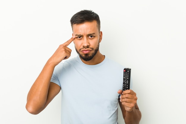 Junger südasiatischer Mann mit einem TV-Controller, der eine Enttäuschungsgeste mit dem Zeigefinger zeigt.