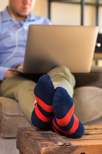 Junger tausendjähriger Geschäftsmann, Freiberufler, der an einem Laptop arbeitet, der auf der Couch sitzt. Lifestyle-Komposition mit natürlichem Licht. Bleiben Sie zu Hause Konzept