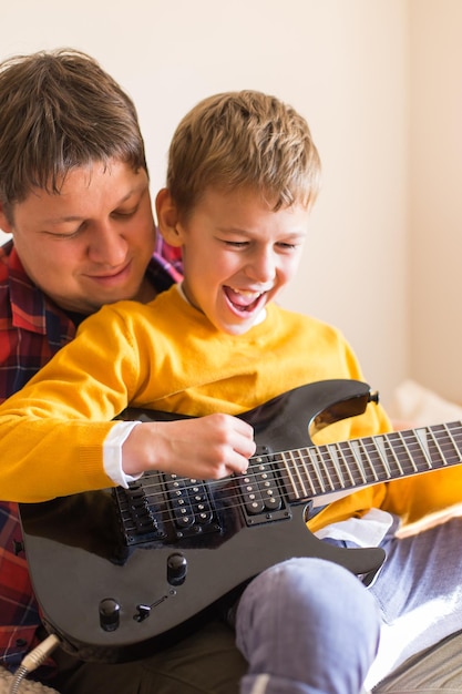 Junger tausendjähriger Mann, Vater und süßer Sohn, der E-Gitarre spielt. Bleiben Sie zu Hause, Aktivitäten zu Hause, Lernkurse, Familie, die gemeinsam Spaß hat