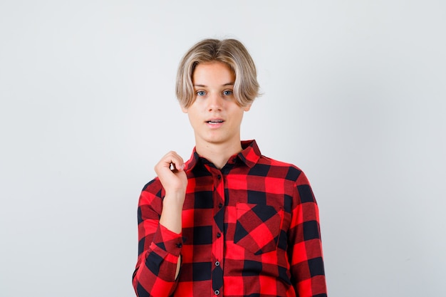 Foto junger teenager, der daumen zurück in kariertes hemd zeigt und selbstbewusst aussieht. vorderansicht.