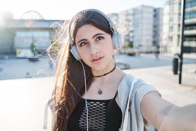 Junger Teenager, der ein Selfie mit einer Handyfrau mit Kopfhörern macht, die einen Videoanruf in der Stadt macht