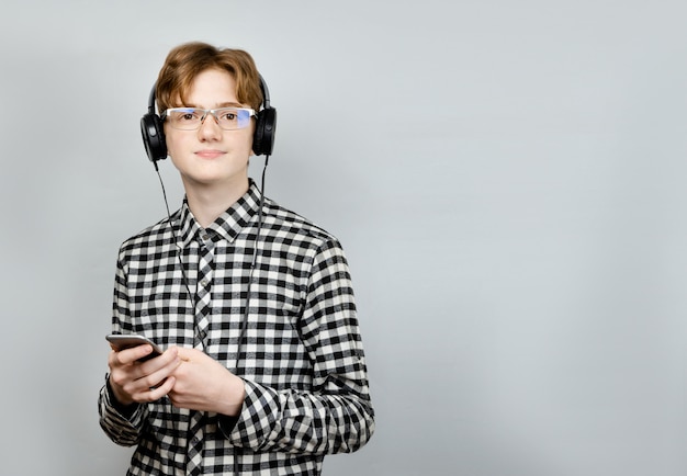 Junger Teenager mit roten Haaren in einem karierten Hemd, in Kopfhörern mit Musik.