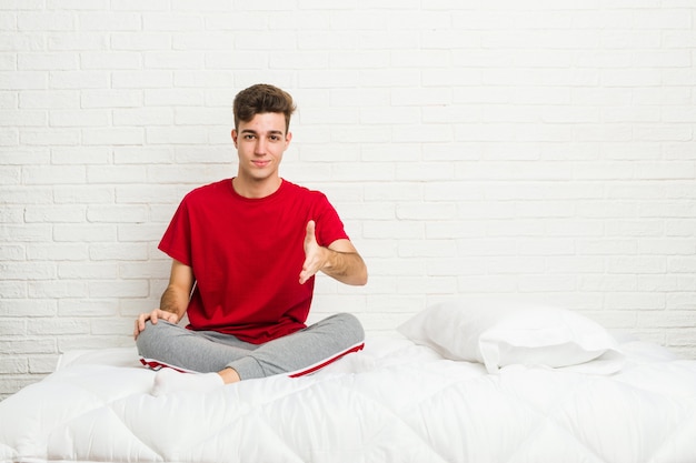 Junger Teenager-Studentenmann auf dem Bett, das Hand streckt
