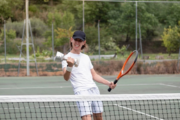 Junger Tennisspieler, der seinen Sieg des Wettbewerbs mit einer Tasse in der Hand und einem glücklichen Gesicht feiert