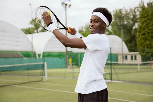 Junger Tennisspieler mit afrikanischem Aussehen übt auf dem Tennisplatz und posiert für Fotos