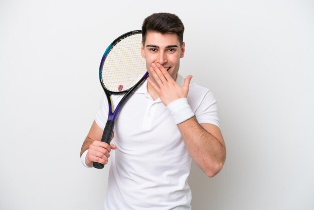 Junger Tennisspielermann lokalisiert auf weißem Hintergrund glücklich und lächelnd, den Mund mit der Hand bedeckend