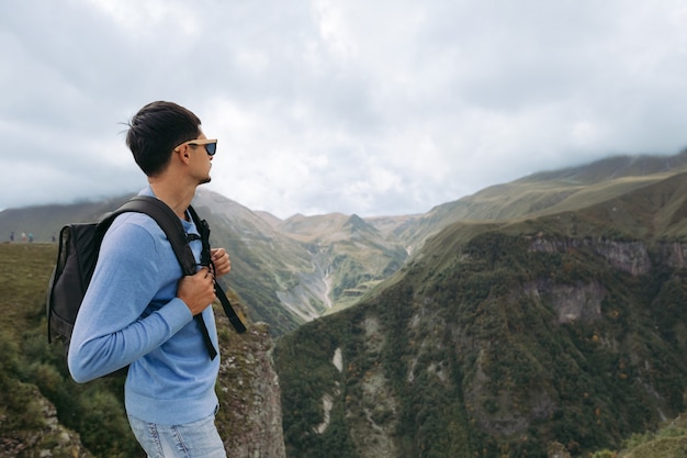 Junger Touristenmann mit einem Rucksack gegen den Hintergrund des Kaukasusgebirges, Georgia an einem nebligen Tag. Speicherplatz kopieren