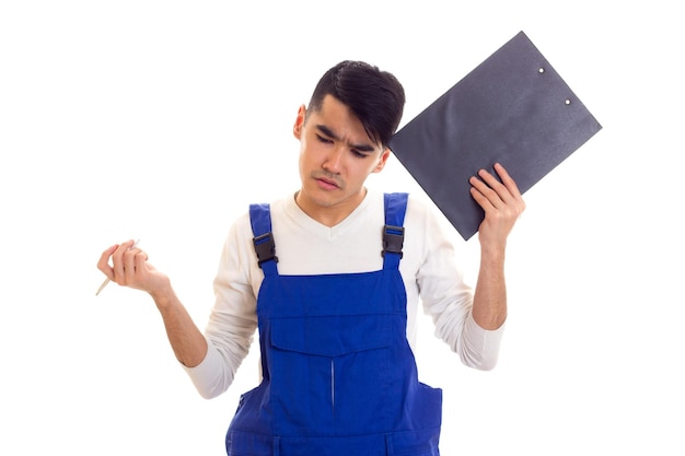 Junger trauriger Mann mit dunklem Haar in Hemd und blauem Overall mit weißem Stift und schwarzem Ordner