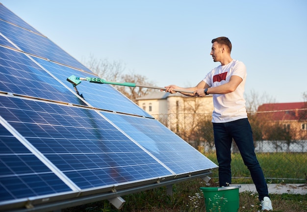 Junger Typ reinigt Solarpanel auf einem Grundstück in der Nähe des Hauses