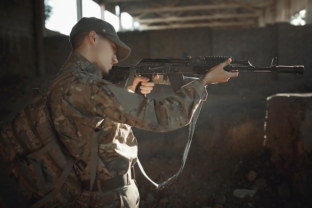 Junger ukrainischer Soldat in Tarnuniform mit Maschinengewehr im zerstörten Gebäude