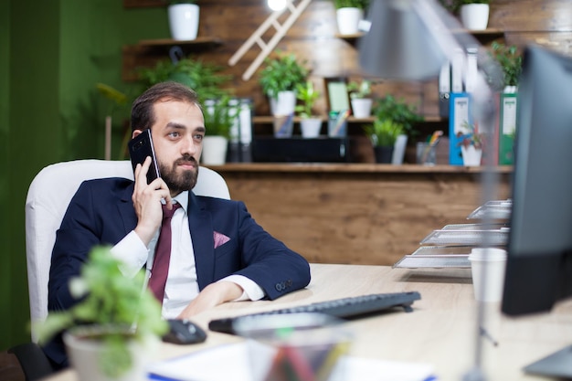 Foto junger und eleganter geschäftsmann, der die daten von seinem monitor überprüft und ein geschäftsgespräch auf seinem handy führt. kluger geschäftsmann.