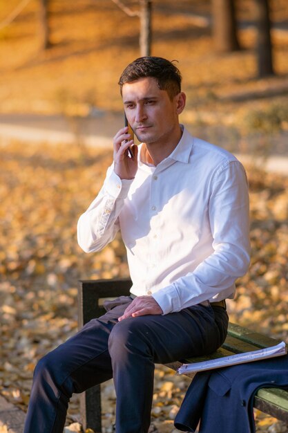 Junger und erfolgreicher Geschäftsmann, der im Park steht und am Telefon spricht.