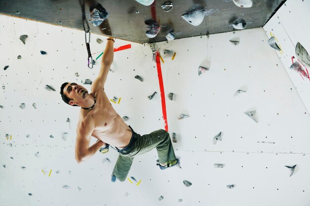 Junger und fitter Mann trainiert freies Bergsteigen an der Indoor-Übungswand