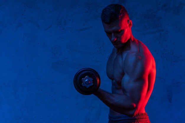 Junger und muskulöser Bodybuilder, der mit einer Hantel in buntem Neonlicht trainiert