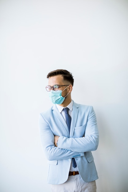 Junger und stilvoller Geschäftsmann mit Gesichtsmaske steht an der Wand im Büro
