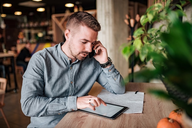 Junger Unternehmer, der über Handy spricht und digitale Tablette verwendet.