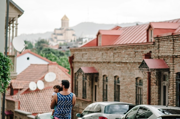 Junger Vater, der an einem sonnigen Frühlingstag mit seiner kleinen Tochter im Freien auf den Straßen der Stadt Tiflis in der Hauptstadt Georgiens spazieren geht Papa und Mädchen reisen auf Exkursion in die Altstadt