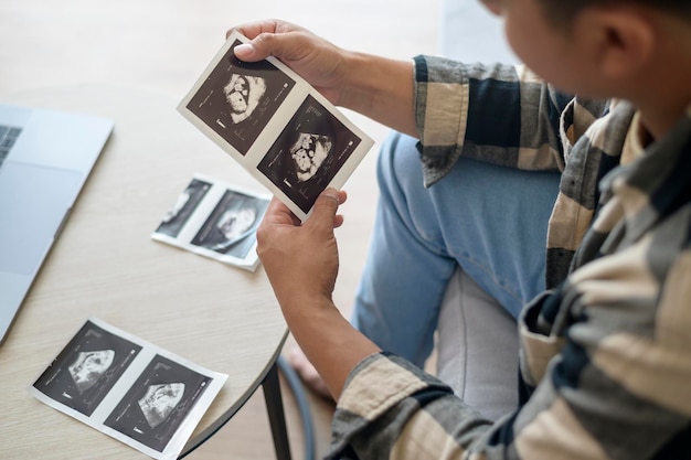 Junger Vater, der ein Ultraschallfoto des neugeborenen Mutterschafts- und Familienkonzepts hält