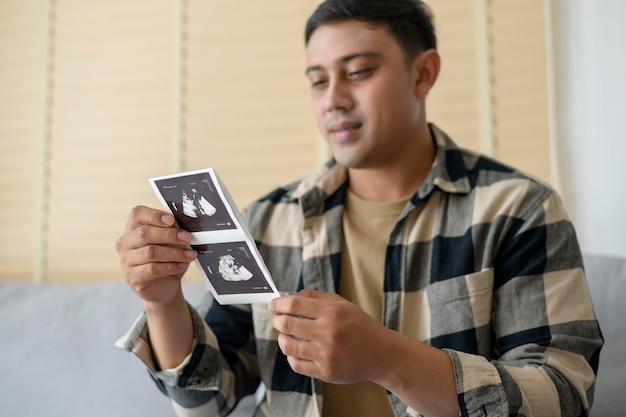 Junger Vater, der ein Ultraschallfoto des neugeborenen Mutterschafts- und Familienkonzepts hält